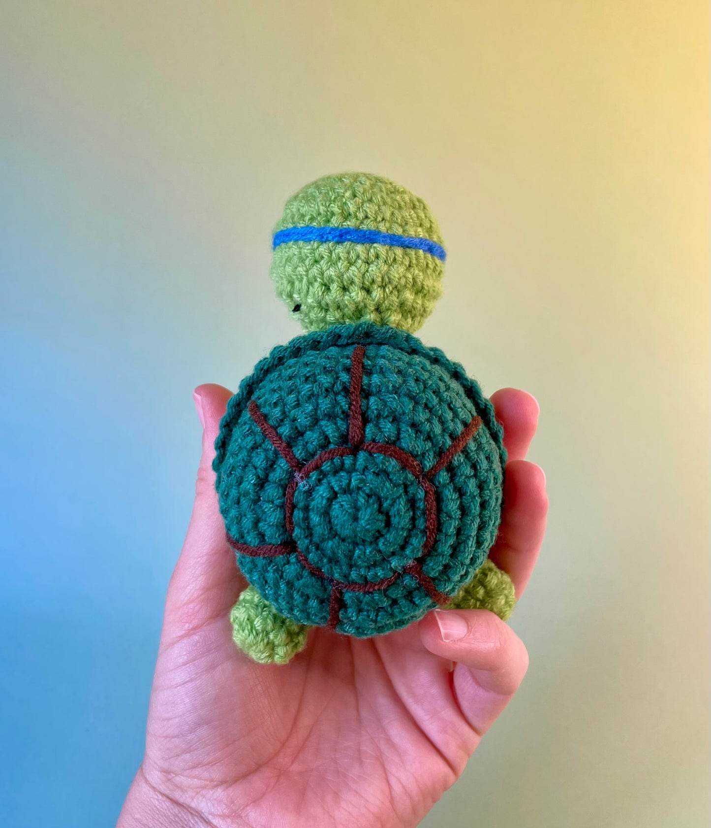 Positive Schildkröte - gehäkelte Figur mit motivierender Botschaft in der Hand gehalten von hinten fotografiert. In Ninja Stil.